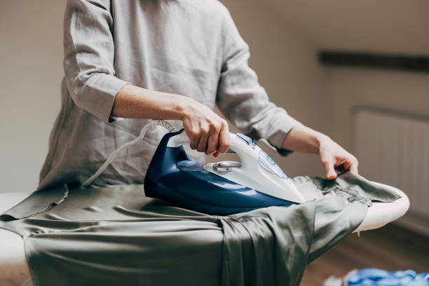 A person carefully irons a green shirt on an ironing board in a cozy, softly lit room, creating a neat and tidy appearance.